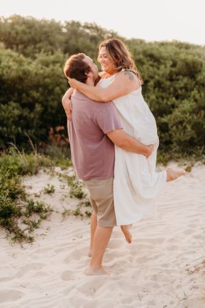 Playful couple sharing a joyful moment on sandy beach dunes.