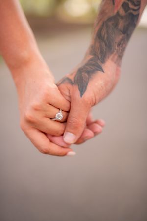 Close-up of hands holding together, showing an engagement ring and tattoo artwork.