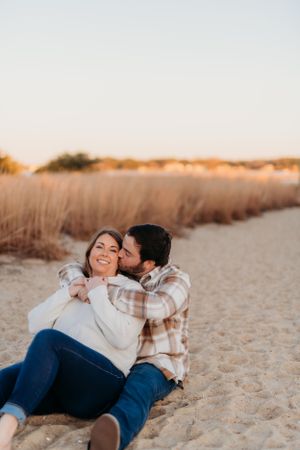 A couple shares a playful moment on a sandy beach during sunset.