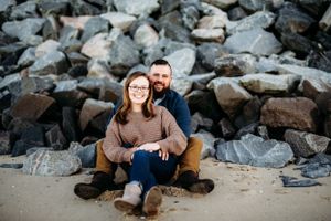 Engagement photo of a couple sitting together on large rocks by the water.