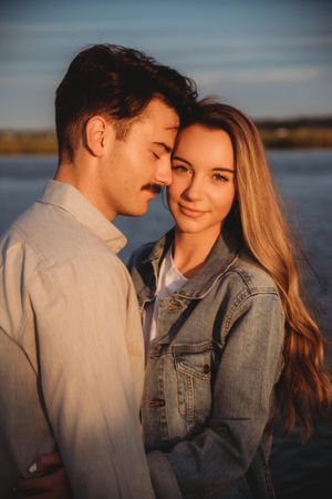 Romantic sunset portrait of couple in casual attire by a lake.
