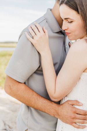 Intimate romantic embrace between couple in light clothing against a sunny outdoor backdrop.