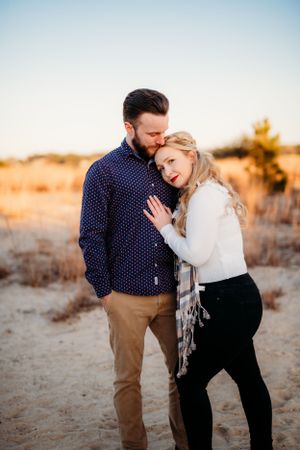 Couple in casual attire embracing during sunset engagement photo session in desert landscape.