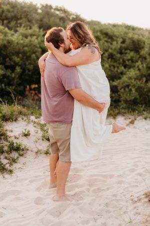 Romantic beach photo of couple embracing against natural foliage backdrop.