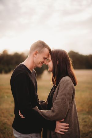 A couple shares an intimate moment while embracing in a field at sunset.