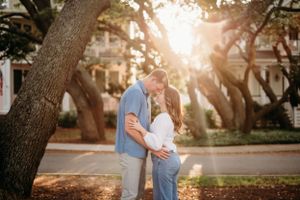 Romantic couple embraces under sun-dappled trees in urban setting.