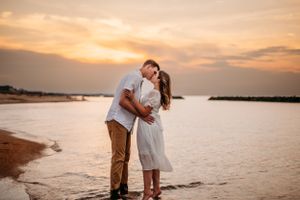 Romantic couple embracing on beach at sunset with orange sky and water in background.