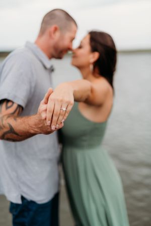 An engaged couple shares an intimate moment by the water while showing off the ring.