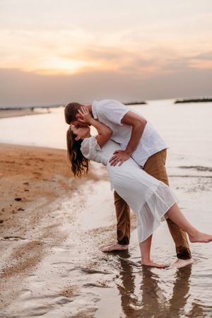 Couple sharing romantic moment at beach during golden hour with waves in background.