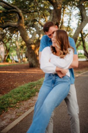 Intimate moment between couple on park pathway with sunlit trees in background.