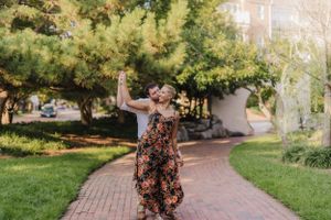 Dancing figure in floral dress twirls joyfully on garden path.
