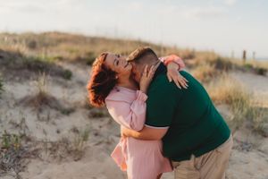 A playful couple sharing a romantic moment among coastal sand dunes.