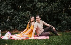 Couple lounging on pink picnic blanket in a park setting.