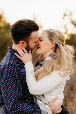 Romantic couple in winter attire sharing intimate moment during golden hour engagement session.