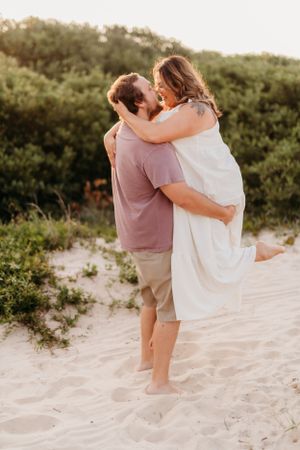 Loving couple embracing on sandy beach dunes during sunset.