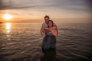 A romantic sunset embrace in the ocean water with golden light reflecting on the calm sea surface.