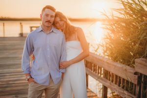 Couple posing on waterfront boardwalk during golden hour photo session.