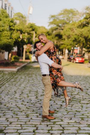 Playful couple embracing on cobblestone street during sunset photoshoot.