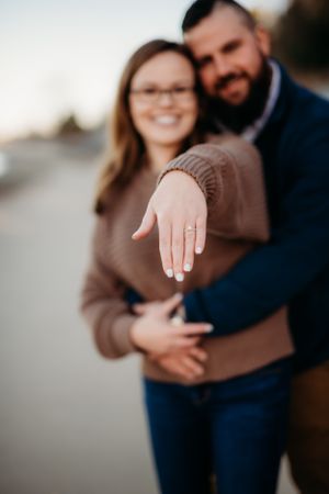 Close up of a hand displaying an engagement ring during a romantic photoshoot at sunset.