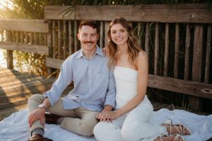 Couple sitting on wooden deck during golden hour engagement session.