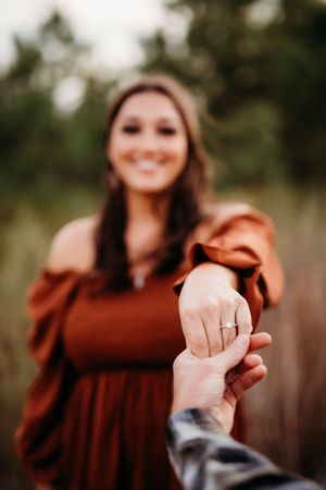 Close up of a woman in a rust-colored sweater showing off her engagement ring.