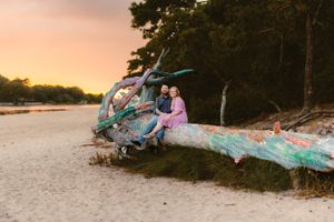 Couple sitting on colorful painted driftwood log at beach during sunset.
