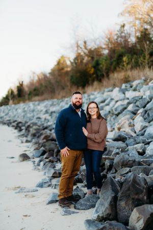 Couple posing against rocky coastal backdrop during engagement photoshoot.