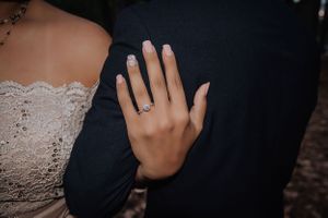 Close-up of engagement ring on hand resting against dark formal attire.
