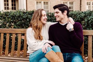 A happy couple sitting together on a wooden bench sharing a laugh near greenery and a stone building.