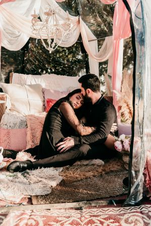 Couple cuddling intimately in a romantic tent setting with draped fabric and soft lighting.