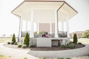 White hexagonal gazebo with landscaped shrubs in a park setting.