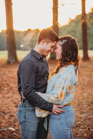 Couple sharing a tender moment in autumn sunlight among fallen leaves.