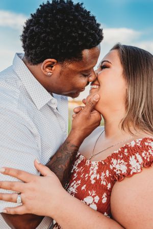 Romantic outdoor engagement photo with sunlit field backdrop.