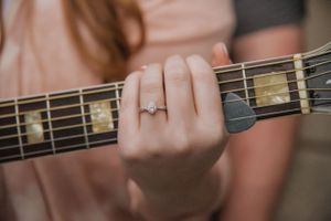 Hand wearing an engagement ring while playing acoustic guitar strings.