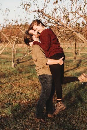 Romantic couple embracing in an autumn orchard during golden hour.
