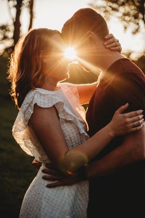 Romantic sunset embrace with sunflare and lace dress details.