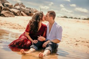 Couple sitting in shallow water sharing romantic moment on sandy beach.