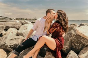 Romantic couple sharing intimate moment on rocky beach during sunset.