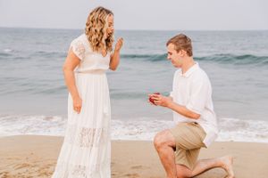 A beachside proposal scene with waves crashing behind two people in white attire on the sand.