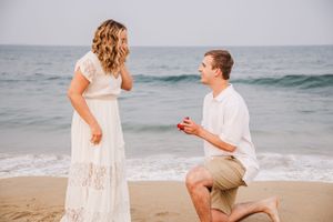 Traditional proposal moment on sandy beach with ocean waves in background.
