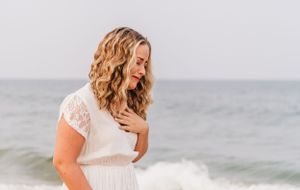 Woman in white dress looks down emotionally during beach proposal.