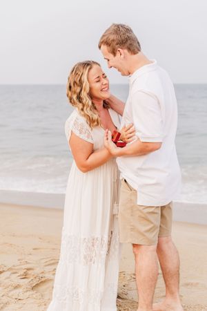 Joyful couple embracing on beach during proposal with ocean backdrop.