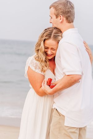 Couple sharing intimate moment on beach during proposal with ring box.
