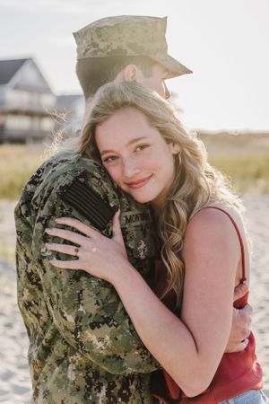 Military homecoming embrace captured on sandy beach at sunset.