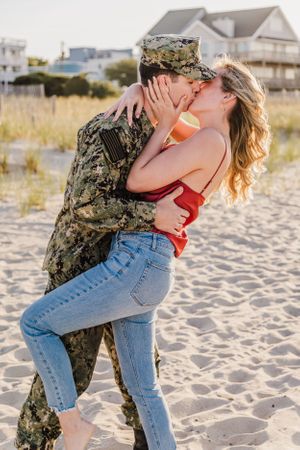 Couple embracing during beach photoshoot with beach houses in background.