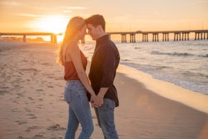 Romantic couple sharing intimate moment on beach at golden sunset with pier in background.