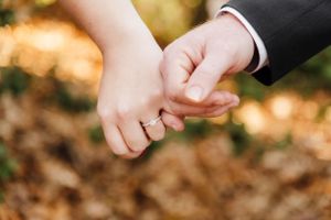 Close up of two hands holding each other against autumn leaves background.