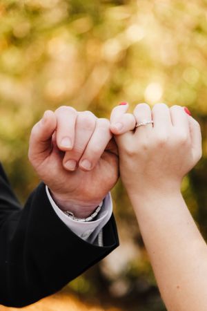 Romantic pinky promise between couple showing wedding rings against autumn background.