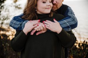Intimate engagement photo showing couple embracing in warm winter clothing at sunset.