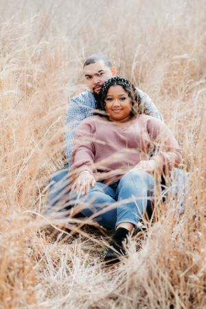 A couple sits together in tall golden grass during a romantic outdoor photo session.